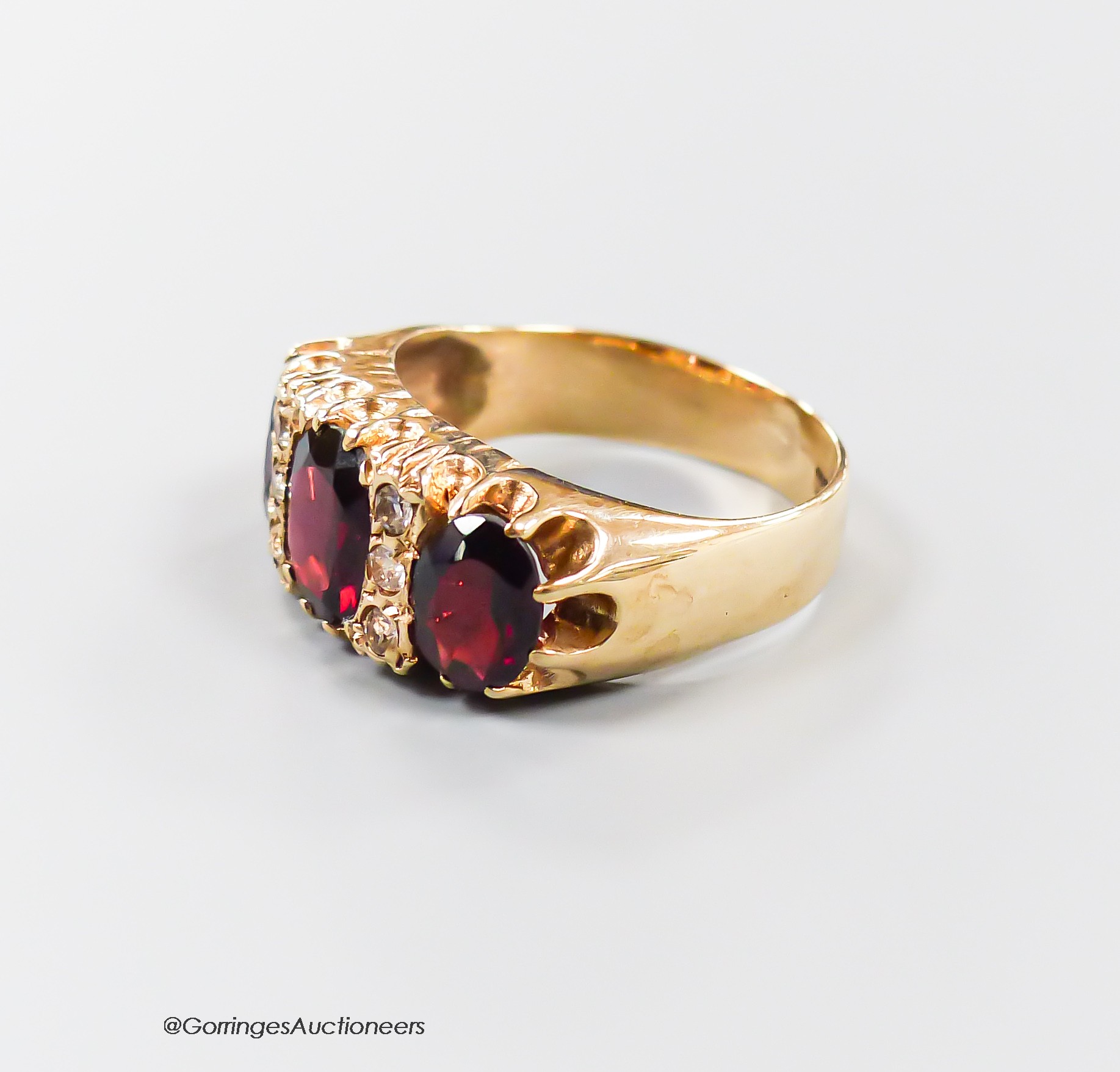 A modern 9ct gold and graduated three stone garnet set half hoop dress ring, with diamond chip spacers, size N, gross 4.9 grams.